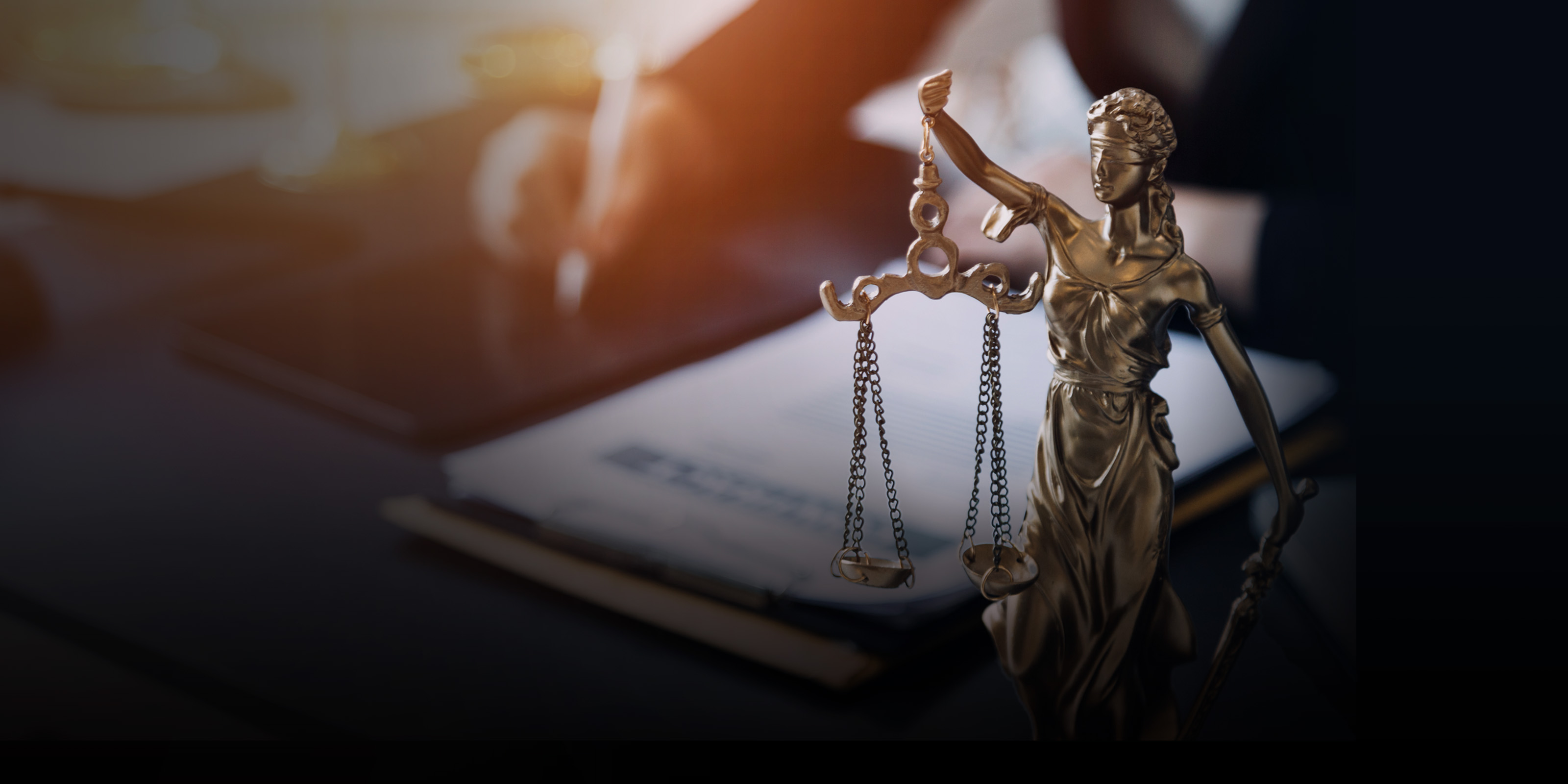 Statue de la justice tenant une balance et, en arrière-plan, un avocat travaillant à un bureau