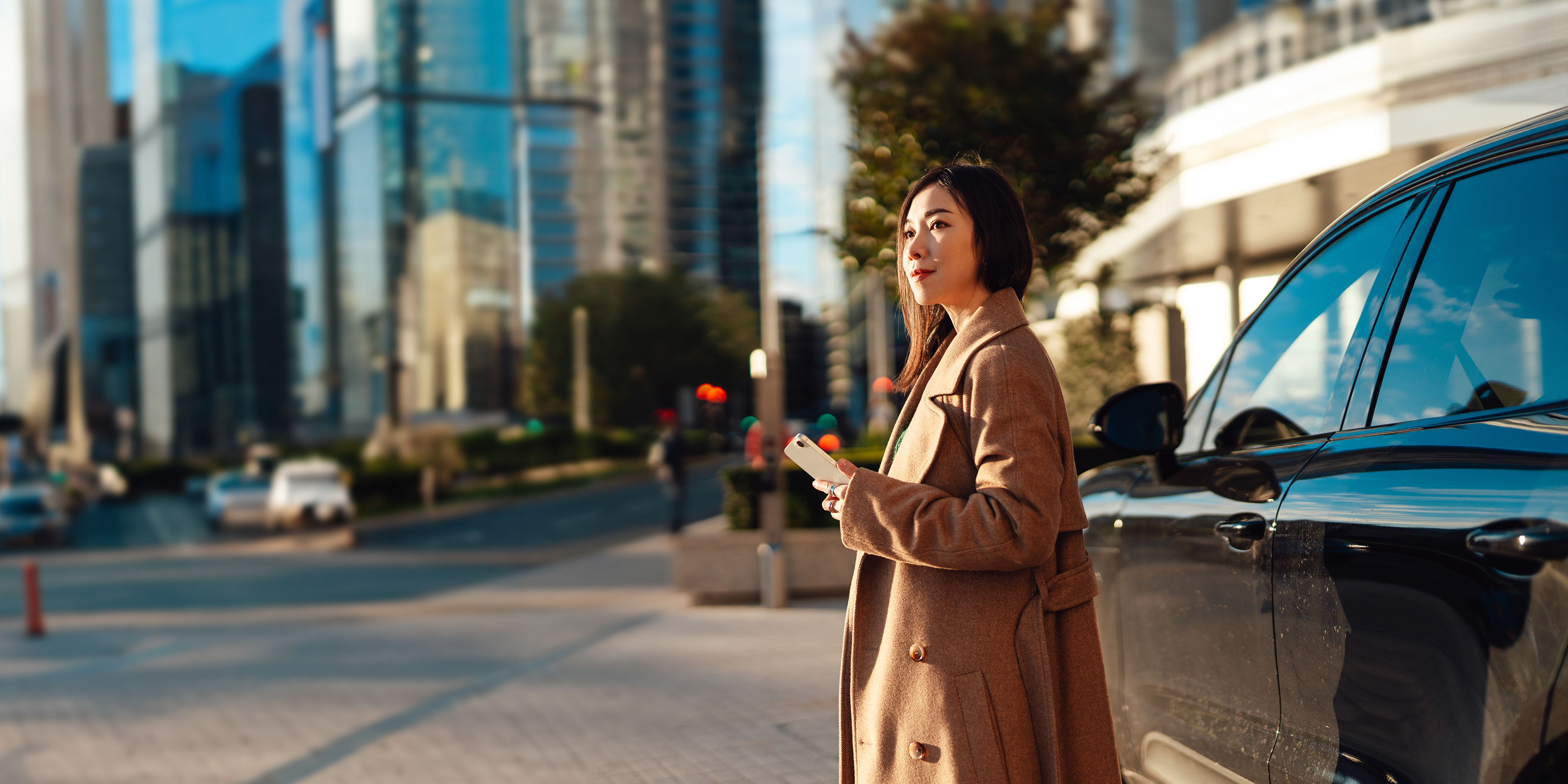 A woman locking her car with a smartphone app in front of her parked car against an urban cityscape.   